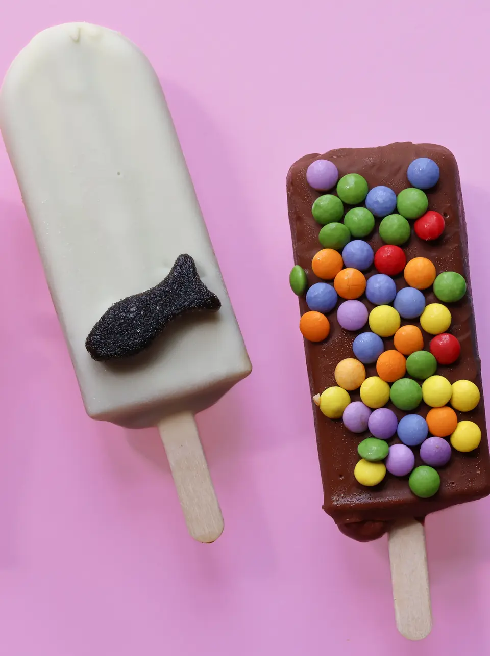 Zwei Eis am Stiel von Popsicle, eins mit Lakritzfisch und eins mit bunten Schokolinsen